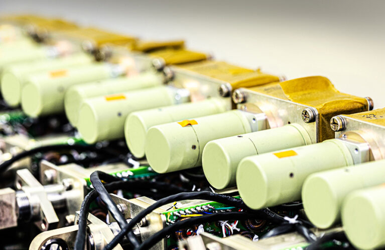 Close-up of a row of electrical components with green cylinders and cable connections arranged in a technical environment.